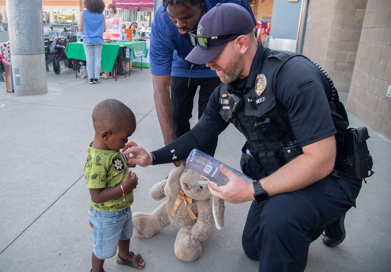 Stockton Police officer Burt Linde, right, gives a sticker to 1-year-old Ajani White at the National Night Out event sponsored by Parents by Choice, the Stockton Ports, San Joaquin Office of Education and the Downtown Stockton Alliance at the Stockton Ballpark in downtown Stockton on Aug. 6, 2024.