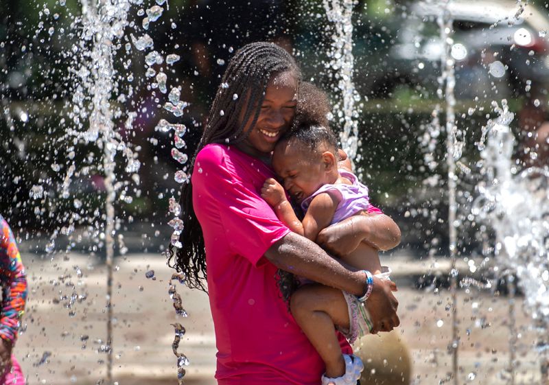 Lee'Onna Thompson, 11, carries her 1-year-old sister Leezariah Daniels to cool off from a triple-digit heat wave in the interactive fountain at the Weber Point Events Center in downtown Stockton on Jun. 4, 2024.