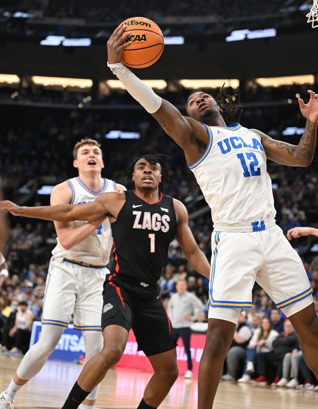 Dec 28, 2024; Inglewood, California, USA; UCLA Bruins guard Sebastian Mack (12) hauls in a rebound in front of forward Tyler Bilodeau (34) and Gonzaga Bulldogs guard Michael Ajayi (1) during the first half at Intuit Dome. Mandatory Credit: Robert Hanashiro-Imagn Images