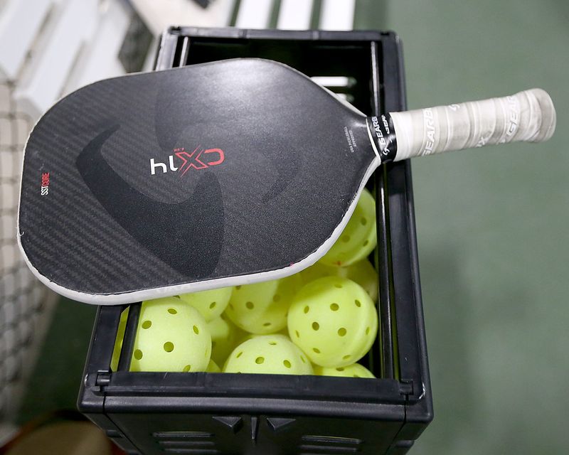 A paddle rests on a cart full of pickleballs for a Coach and Play lesson at Pickles in Hanover, a Pickleball indoor court facility, on Thursday, June 30, 2022.