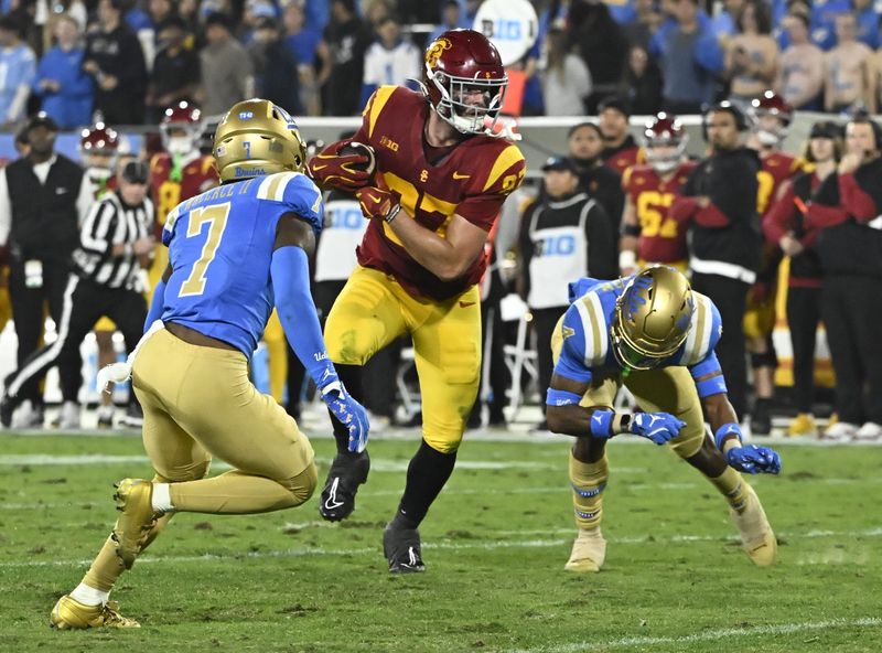 Nov 23, 2024; Pasadena, California, USA; USC Trojans tight end Lake McRee (87) runs a pass between UCLA Bruins defensive back K.J. Wallace (7) and defensive back Bryan Addison (4) during the second quarter at Rose Bowl. Mandatory Credit: Robert Hanashiro-Imagn Images