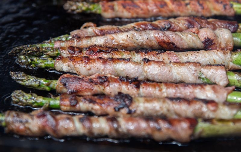 Bacon-wrapped asparagus is cooked by Jasmine Camello at the annual Asparagus Festival at the San Joaquin County Fairgrounds in Stockton on Apr. 11, 2025.