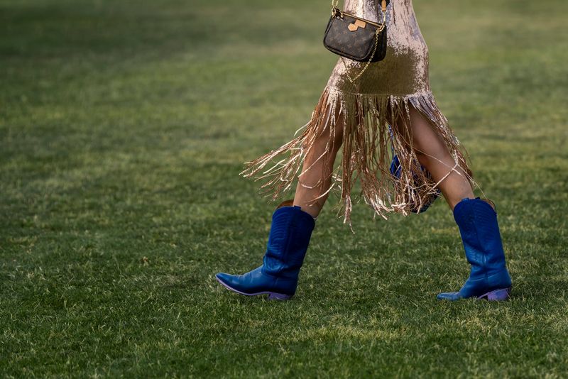 A festivalgoer walks between venues in blue cowboy boots during the Coachella Valley Music and Arts Festival in Indio, Calif., Saturday, April 12, 2025.