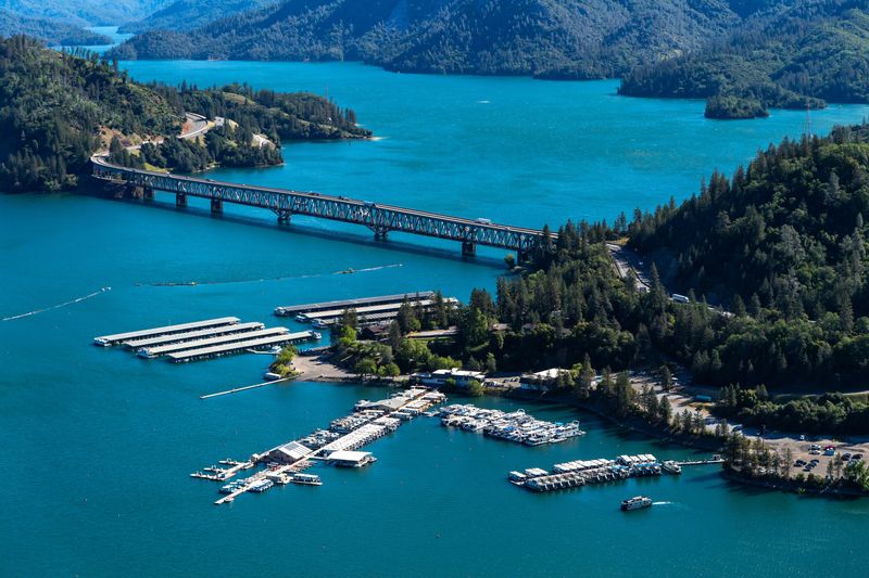 An aerial view of Pit River Bridge that spans Lake Shasta and the adjacent marina in Shasta County, California on May 9, 2024. On this date, the reservoir storage was 4,380,600 acre-feet (AF), 96 percent of the total capacity. Operated by the U.S. Department of the Interior Bureau of Reclamation, Shasta Dam backs up water from the Sacramento River for more than 35 miles to form the lake and controls flood waters, while supplying water for irrigation, municipal and industrial use, wildlife habitat maintenance and power generation.