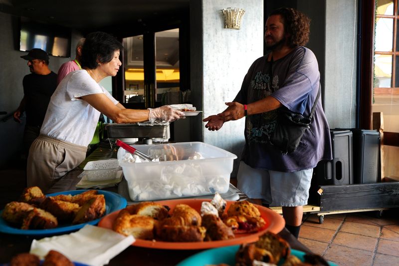 Well in the Desert volunteer Grace Reyes, left, hands a hot meal to Raul Rivera inside Oscar's in downtown Palm Springs, Calif., on Wed., July 16, 2025.