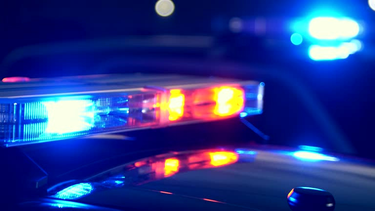 Emergency lights flashing on police cars at night at the scene of an accident or crime. Focus shifts from lights in the foreground to the lights in the background.