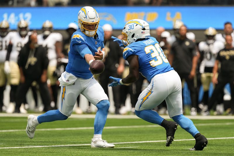 Aug 10, 2025; Inglewood, California, USA; Los Angeles Chargers quarterback Taylor Heinicke (4) hands the ball off to running back Kimani Vidal (30) against the New Orleans Saints at SoFi Stadium. Mandatory Credit: Jon Endow-Imagn Images