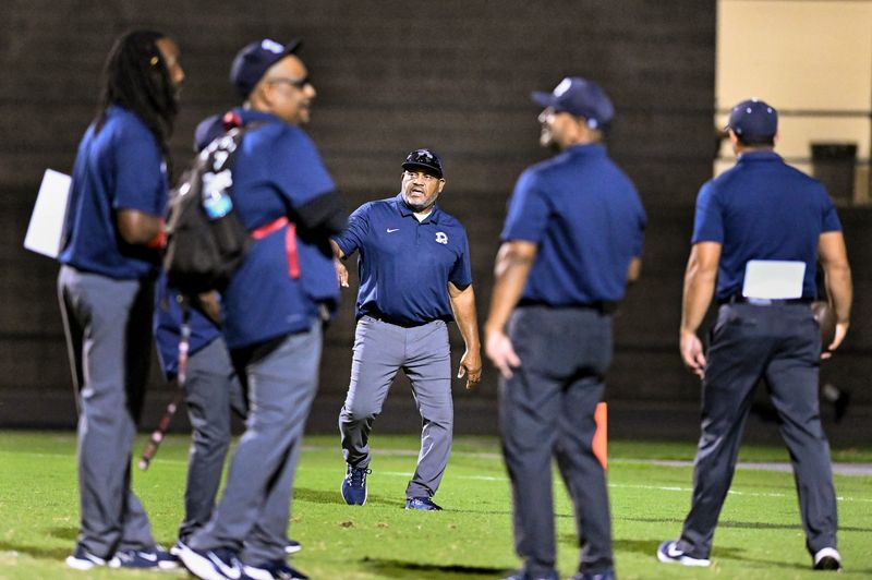 Redwood’s Head Coach Curtis Allen, center, talks with his assistants before their game against Hanford in non-league high school football Friday, September 19, 2025.
