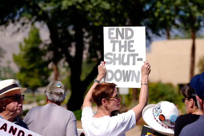 Angela Cole of Palm Springs holds a sign reading "END THE SHUT-DOWN" while protesting outside the district office of GOP Rep. Ken Calvert in opposition to the federal government shutdown and the Trump administration in Palm Desert, Calif., on Wednesday, October 1, 2025.