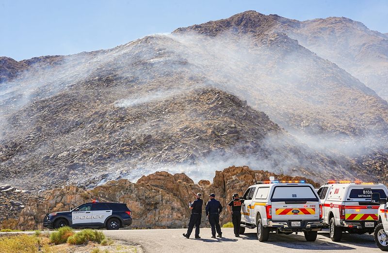 Responders from the Palm Springs Fire, Cal Fire and the Palm Springs Police Department converge on a fire burning in the foothills near the Ship Rock formation, foreground, along Hwy 111 in Palm Springs, Calif., Oct. 18, 2025.