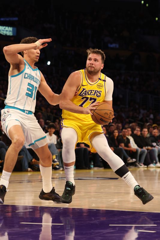 Feb 19, 2025; Los Angeles, California, USA; Los Angeles Lakers guard Luka Doncic (77) drives against Charlotte Hornets forward Tidjane Salaun (31) during the second quarter at Crypto.com Arena. Mandatory Credit: Jason Parkhurst-Imagn Images