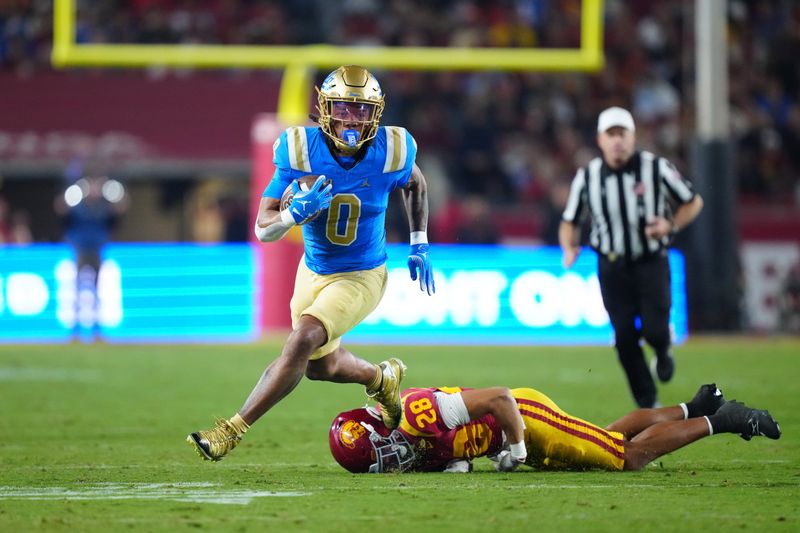 Nov 29, 2025; Los Angeles, California, USA; UCLA Bruins running back Jalen Berger (0) carries the ball against Southern California Trojans safety Kennedy Urlacher (28) in the first half at United Airlines Field at Los Angeles Memorial Coliseum. Mandatory Credit: Kirby Lee-Imagn Images