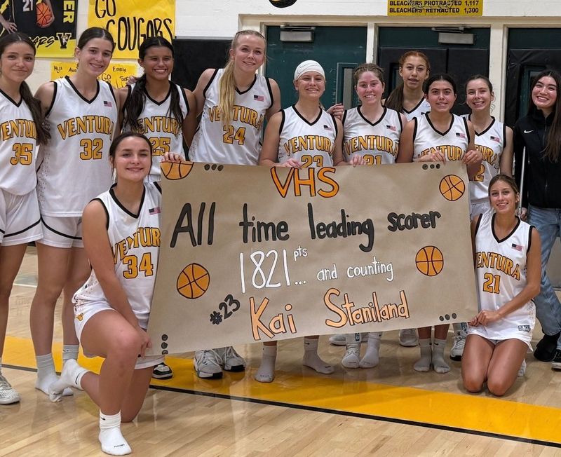 Ventura High girls basketball star Kai Staniland (23) poses for a photo with her teammates and a sign celebrating her setting the all-time career scoring record at Ventura High during a win over San Marcos on Jan. 6 at home.