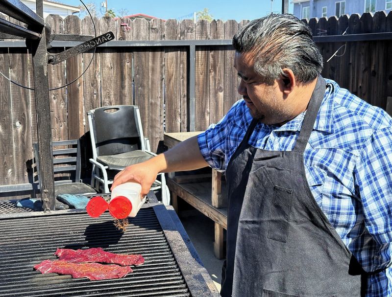Oldest son Tako Sierra, the grill master of Tacos Las Espadas, adds seasoning to meat while it’s grilled using mesquite wood on March 19, 2026.