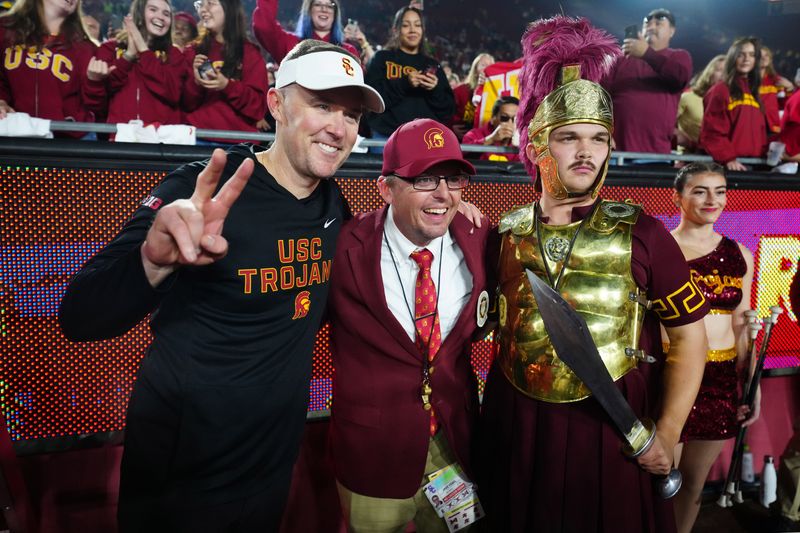 Nov 29, 2025; Los Angeles, California, USA; Southern California Trojans head coach Lincoln Riley (left) poses with Spirit of Troy marching band director James Vogel (center) and mascot Tommy Trojan after the game against the UCLA Bruins at United Airlines Field at Los Angeles Memorial Coliseum. Mandatory Credit: Kirby Lee-Imagn Images