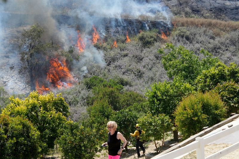 A female homeowner inspects her property as a firefighter battles the Sandy Fire in Simi Valley on May 18, 2026.