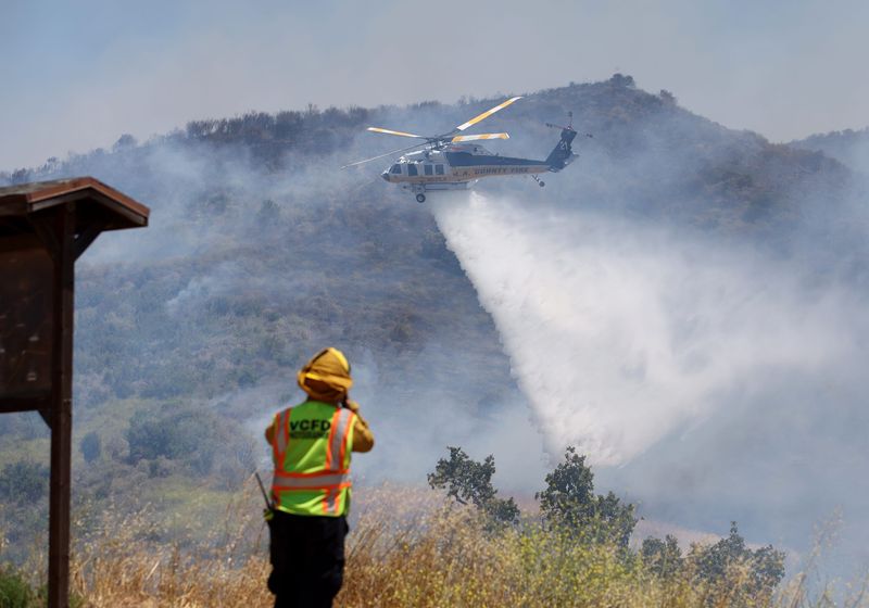 One of the L.A. County Fire helicopters comes in for a drop water on the fire line near homes on Meander Drive in Simi Valley. The Sandy Fire started on May 18, 2026.
