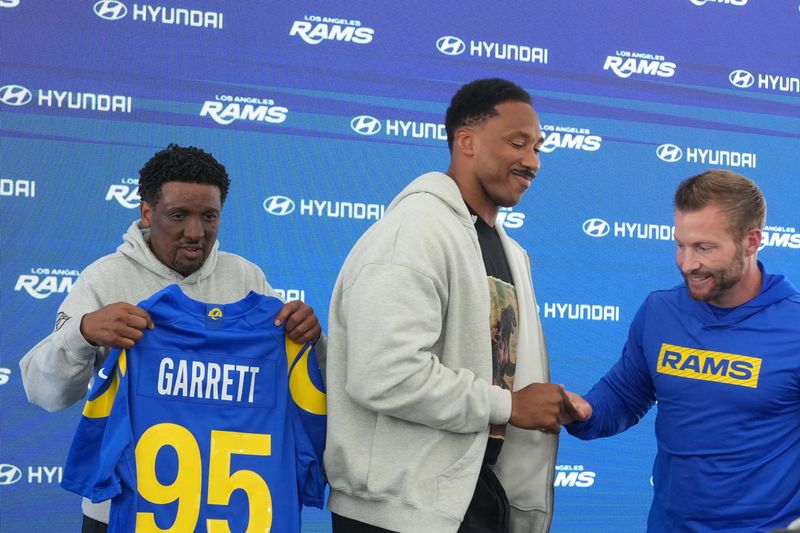 Jun 2, 2026; Woodland Hills, CA, USA; Los Angeles Rams defensive end Myles Garrett (center) is presented a jersey by communications vice president Artis Twyman (left) and coach Sean McVaey during organized team activities at Rams Practice Facility. Mandatory Credit: Kirby Lee-Imagn Images