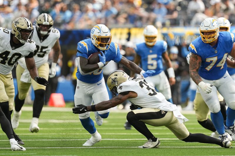 Aug 10, 2025; Inglewood, California, USA; Los Angeles Chargers running back Hassan Haskins (28) runs the ball and is tacked by New Orleans Saints safety Jonas Sanker (33) at SoFi Stadium. Mandatory Credit: Jon Endow-Imagn Images
