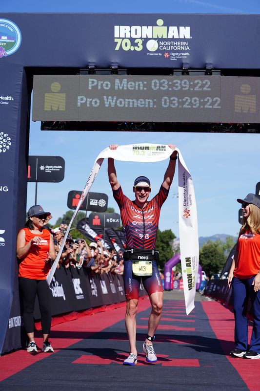 Jason West, the men's winner of the IRONMAN 70.3 Northern California race celebrates by holding up the finish line tape in Redding, California. The Sunday, Aug. 16, 2026 competition began with a 1.2-mile long open swim at Whiskeytown Lake west of Redding. After, the triathletes cycled 56 miles on a course that took them through parts of Redding and Shasta County. They finished with a 13.1-mile run along the Sacramento River Trail.