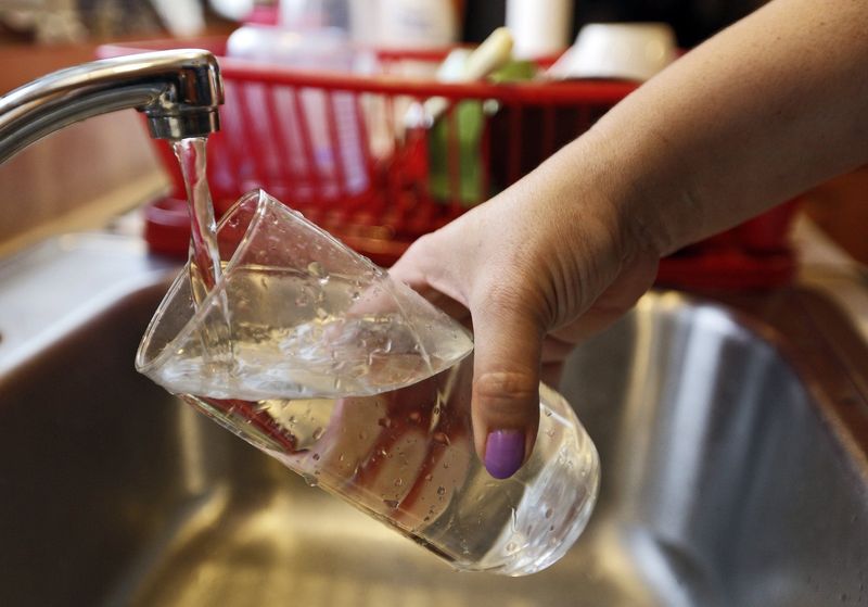Cindy Hairston, of Zanesville, pours a glass of water from the faucet in the kitchen of her parents' home in Zanesville, Ohio, on Sunday, Feb. 9, 2014.