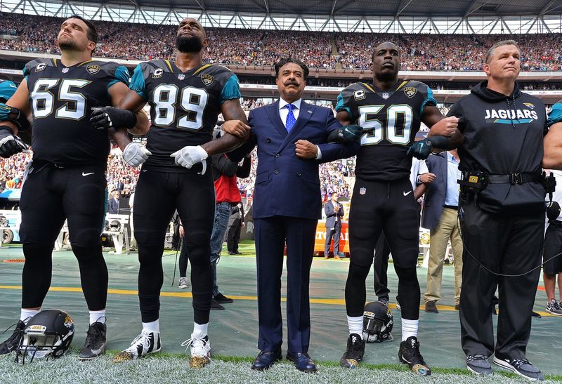 Jacksonville Jaguars team owner Shad Khan (center) and head coach Doug Marrone stand united arm-in-arm with players Brandon Linder (65) Marcedes Lewis (89) and Telvin Smith (50) on the sideline during the singing of the American national anthem before kick-off against the Baltimore Ravens in an NFL game Sunday, September 24, 2017 in London, U.K.