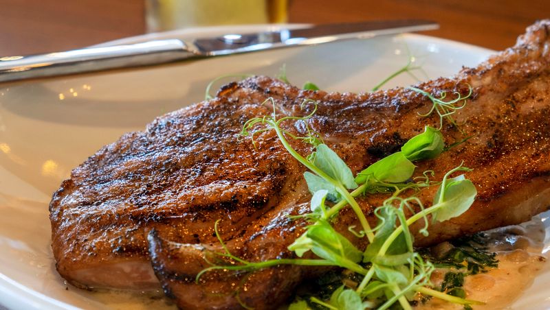 A brined pork chop is among the entrees on the menu at Ember & Iron, the live-fire hearth, ember-roasted restaurant concept from Chef Michael and Brittany Cooney.
