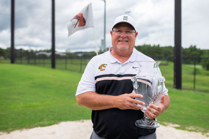 Florida A&M men’s golf head coach Mike Rice poses on the driving range with the championship trophy.