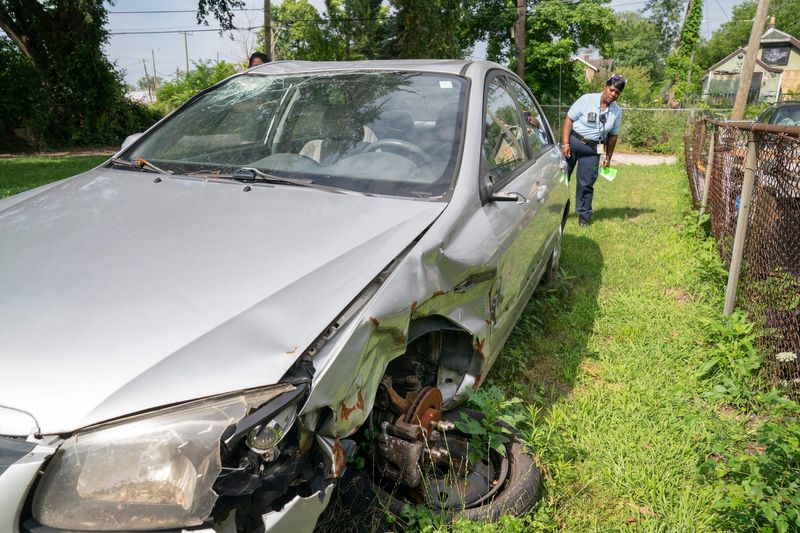 Benta Dixon, City of Detroit Code Enforcement Specialist, inspects a broken down vehicle that is sitting on Detroit Land Bank Authority property on Marx Street in Detroit as she helps residents on Wednesday, July 17, 2024 understand that junk cars can not be left abandoned or left unregistered and in disrepair in their driveways and lawns as mentioned in Mayor Mike Duggan's State of the City address, an initiative to help remove said vehicles to help beautify the city.