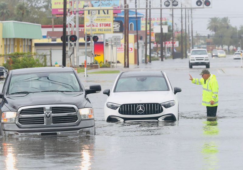 A worker directs traffic through flood waters along International Speedway Boulevard and Segrave Street in Daytona Beach on Thursday, Oct. 10, 2024.