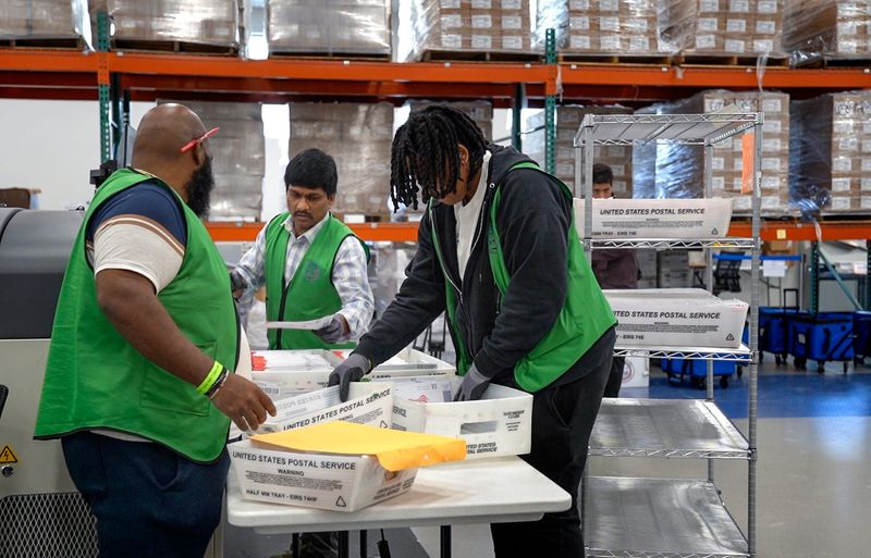 Election workers gather ballots delivered by the postal service to place into a sorting machine at the Palm Beach County Supervisor of Elections office on October 31, 2024, in West Palm Beach, Florida.