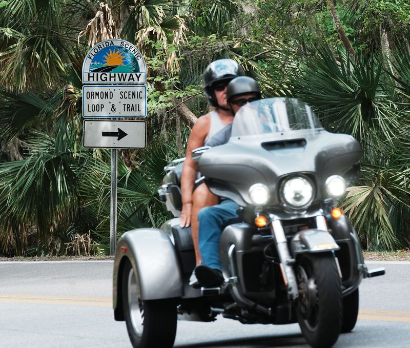 A couple on a motorcycle roll past one of the Ormond Scenic Loop & Trail signs, as they head south through the loop on Old Dixie Highway, Tuesday, April 1, 2025.