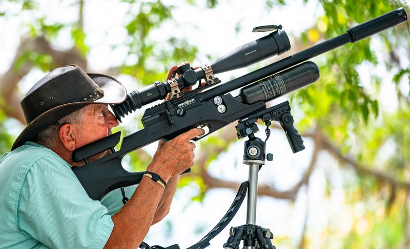 John Johnson, owner of Down Goes Iguana, aims his .25 caliber air rifle at a pair of trees where he's spotted iguanas behind a home on Marco Island, Fla., on Monday, April 7, 2025. Due to the thickets iguanas like to hang out in, he often can't recover their bodies, but he said vultures often find them.