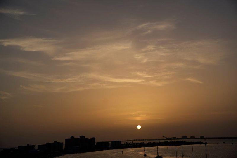 The sun sets over the Sanibel Causeway on Sunday, June 8, 2025. Saharan dust is still lingering over Florida. The dust makes the sky hazy which subdues the brightness of the sun as it sets. It The dust can affect those with respiratory issues. It also suppresses tropical activity and can weaken hurricanes. Photographed from the Fort Myers Beach bridge.