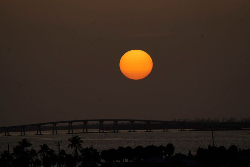 The sun sets over the Sanibel Causeway on Sunday, June 8, 2025. Saharan dust is still lingering over Florida. The dust makes the sky hazy which subdues the brightness of the sun as it sets. It The dust can affect those with respiratory issues. It also suppresses tropical activity and can weaken hurricanes. Photographed from the Fort Myers Beach bridge.
