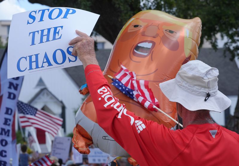 A protester beats a Baby Trump ballon with his American flag at the No Kings protest in front of Daytona Beach City Hall, Saturday June 14, 2025.