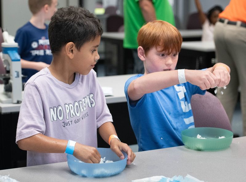 Dylan Pease, left, and Owen Robertson make faux snow as a science experiment during Kids College summer camp at Pensacola State College on June 17, 2025.