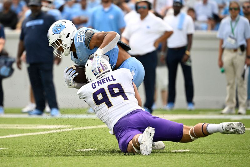 Sep 21, 2024; Chapel Hill, North Carolina, USA; North Carolina Tar Heels running back Omarion Hampton (28) is tackled by James Madison Dukes defensive lineman Eric O'Neill (99) in the second quarter at Kenan Memorial Stadium. Mandatory Credit: Bob Donnan-Imagn Images