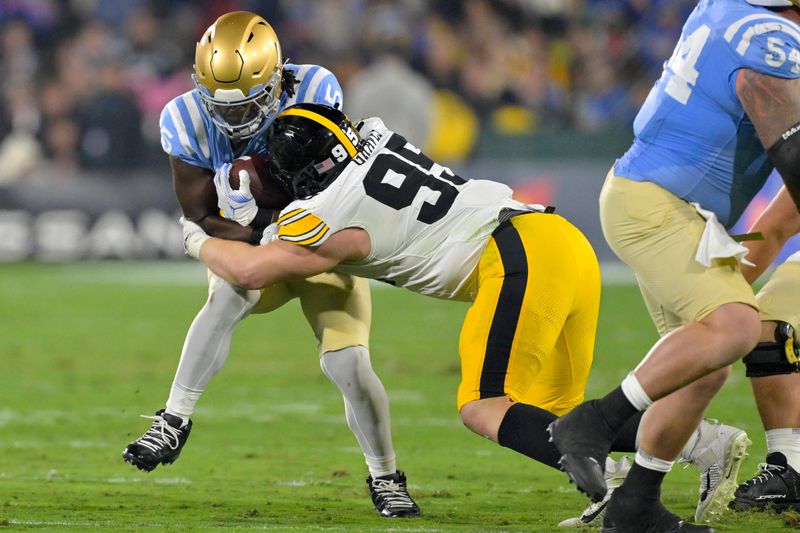 Nov 8, 2024; Pasadena, California, USA; UCLA Bruins running back T.J. Harden (25) is stopped by Iowa Hawkeyes defensive lineman Aaron Graves (95) after a first down in the first half at the Rose Bowl. Mandatory Credit: Jayne Kamin-Oncea-Imagn Images