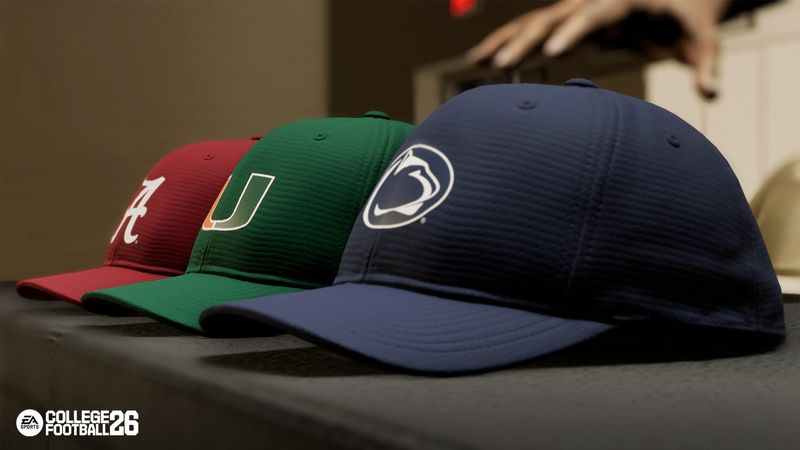 An Alabama, Miami and Penn State hat lie on a table as a player decides which school he will attend in EA Sports College Football 26 road to glory mode.