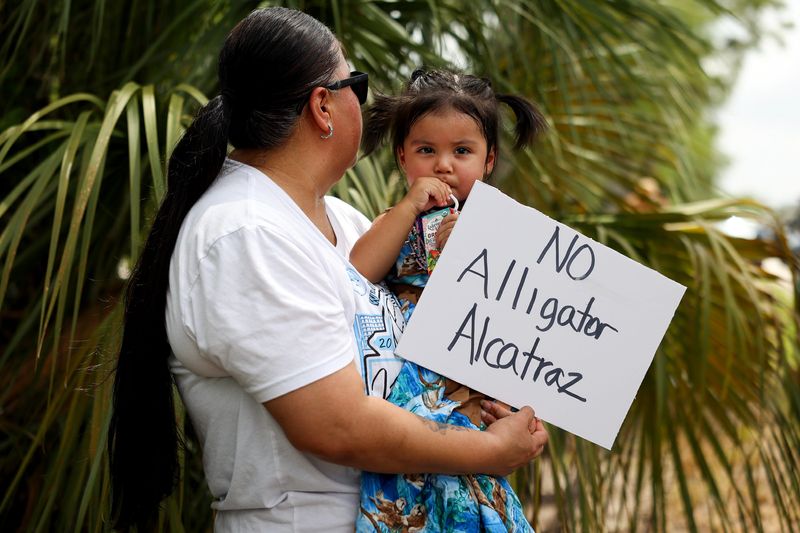 People gather in front of the access road into the Dade-Collier Training and Transition Airport to protest the construction of an immigrant detention center in the Big Cypress Wildlife Management Area on Saturday, June 28, 2025. The demonstration was led by Betty Osceola, an activist and a Miccosukee tribe member. A steady stream of trucks were seen going into the location. The location is being referred to as "Alligator Alcatraz."