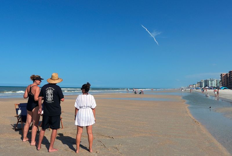 Beachgoers on New Smyrna Beach briefly pause to watch the lift-off of a SpaceX Falcon 9 rocket from Kennedy Space Center, Tuesday, July 1, 2025.