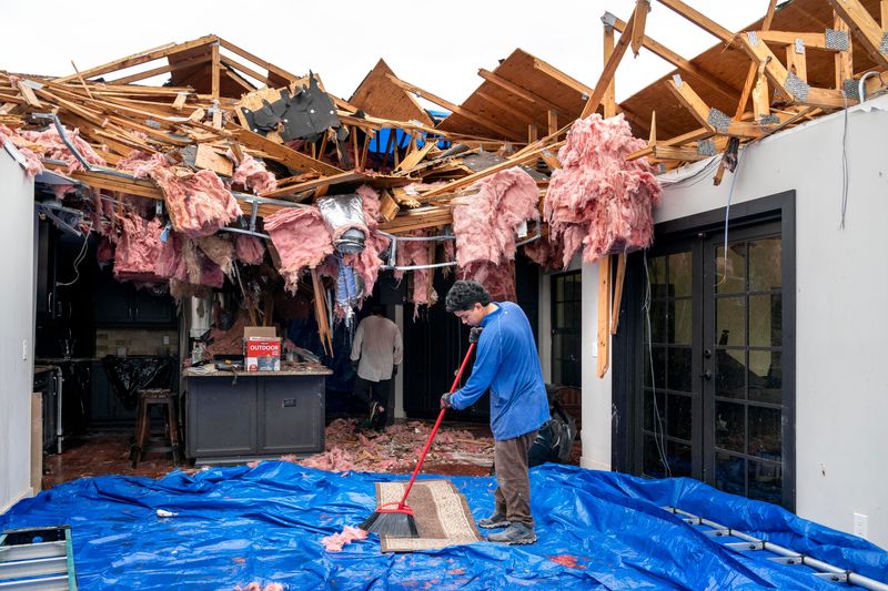Gonzalo Castro sweeps off a rug as he and his family lend a hand to help clean up. Sam Rider and his son Geronimo Rider were inside this home when a tornado spawned by Hurricane Milton ripped off the roof on Wednesday. The father and son were not injured. Friends helped the family on October 11, 2024 in Wellington, Florida.