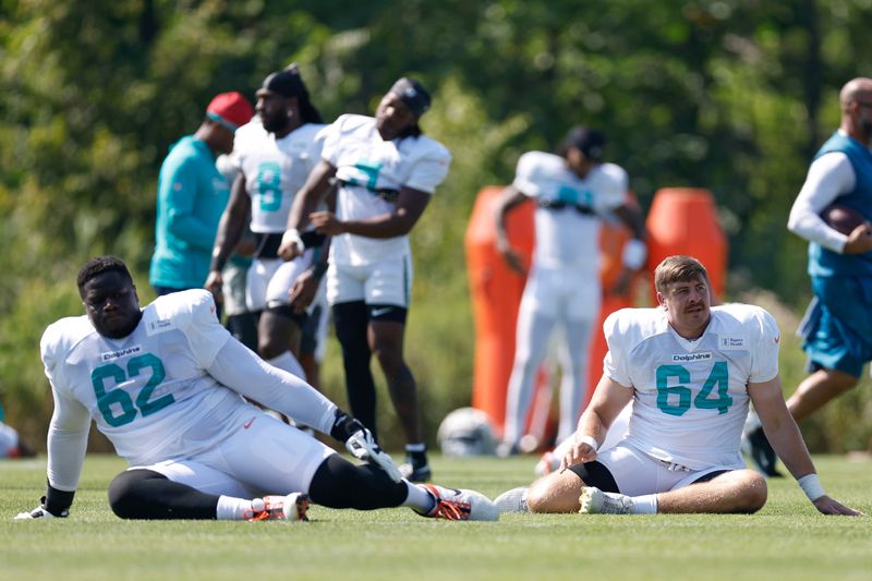Aug 8, 2025; Lake Forest, IL, USA; Miami Dolphins guard Germain Ifedi (62) and offensive tackle Daniel Brunskill (64) stretch during joint training camp practice with the Chicago Bears ahead of Sunday's preseason opener. Mandatory Credit: Kamil Krzaczynski-Imagn Images