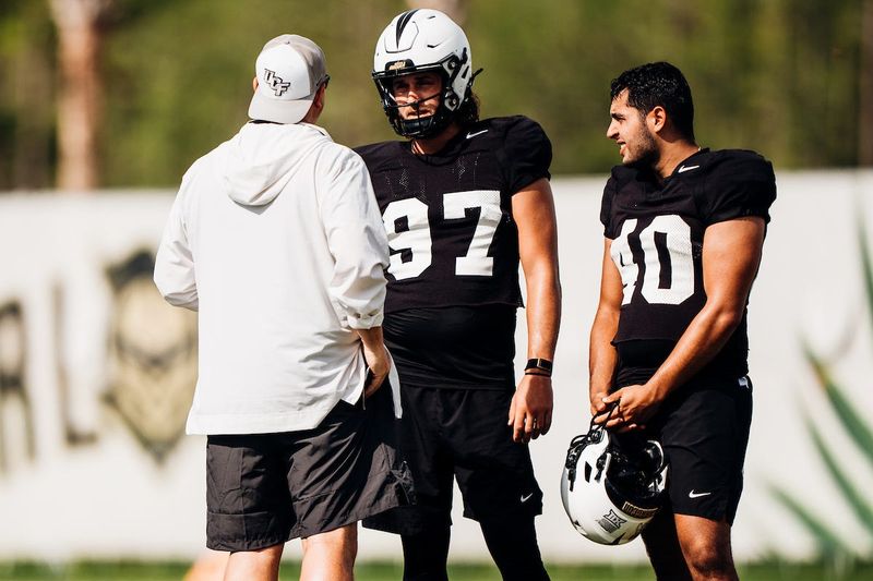 UCF punters Mason Denaburg (97) and Anthony Venneri (40) talk with a coach during a fall practice.