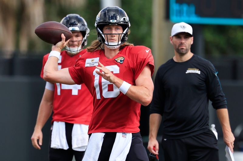 Jacksonville Jaguars quarterback Trevor Lawrence (16) looks to pass as quarterback Nick Mullens (14), left, and quarterbacks coach Spencer Whipple looks on during an NFL training camp session at the Miller Electric Center, Thursday, Aug. 14, 2025 in Jacksonville, Fla.