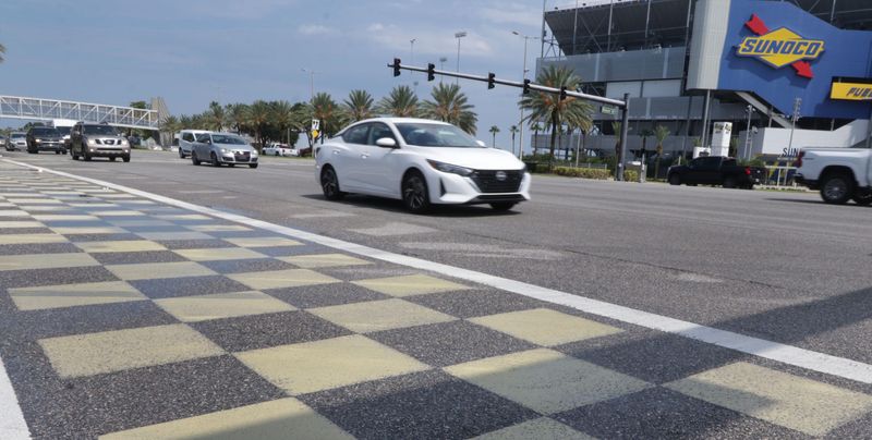 Traffic rolls past one of the checkered-flag crosswalks outside Daytona International Speedway on International Speedway Boulevard in Daytona Beach. Speedway officials confirm that they have been notified by FDOT of its intention to paint over the design as part of a statewide policy.