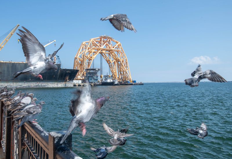 Birds take flight as a massive lift vessel looms over the Port of Pensacola as seen from Plaza de Luna in downtown Pensacola on Sept. 8, 2025. The yellow, arch-shaped structure that is used in offshore oil operations was also seen in the port in October 2019.