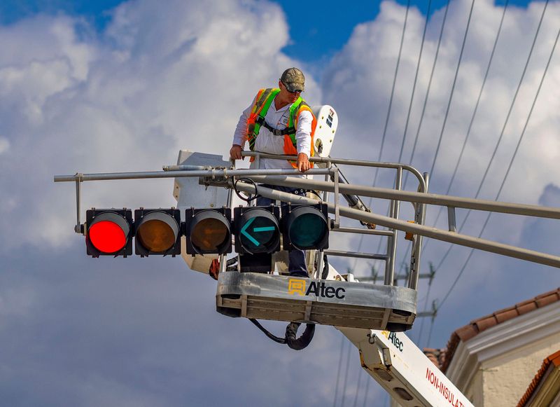 Mark Miller, from the Town of Palm Beach department of public works, talks with a colleague while working to change out a light bulb in the traffic signal at the intersection of N. County Rd. and Royal Poinciana Way April 4, 2023.