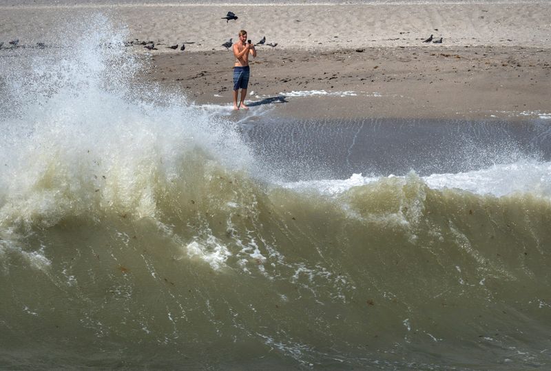 A beachgoer takes photos of the waves crashing as Tropical Storm Imelda makes its way north on September 29, 2025, in Juno Beach, Florida.